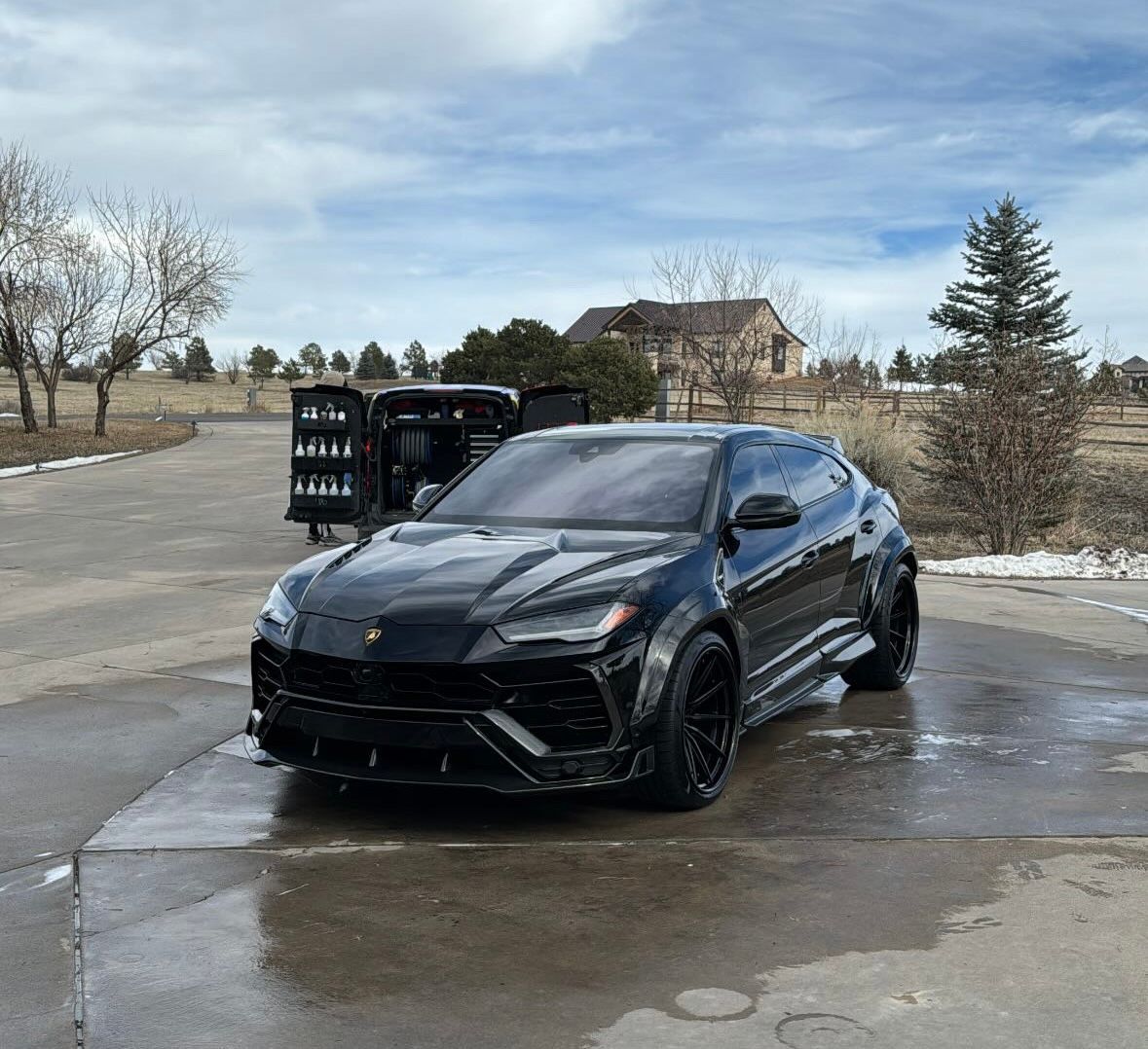 A black lamborghini urus is parked in a parking lot.