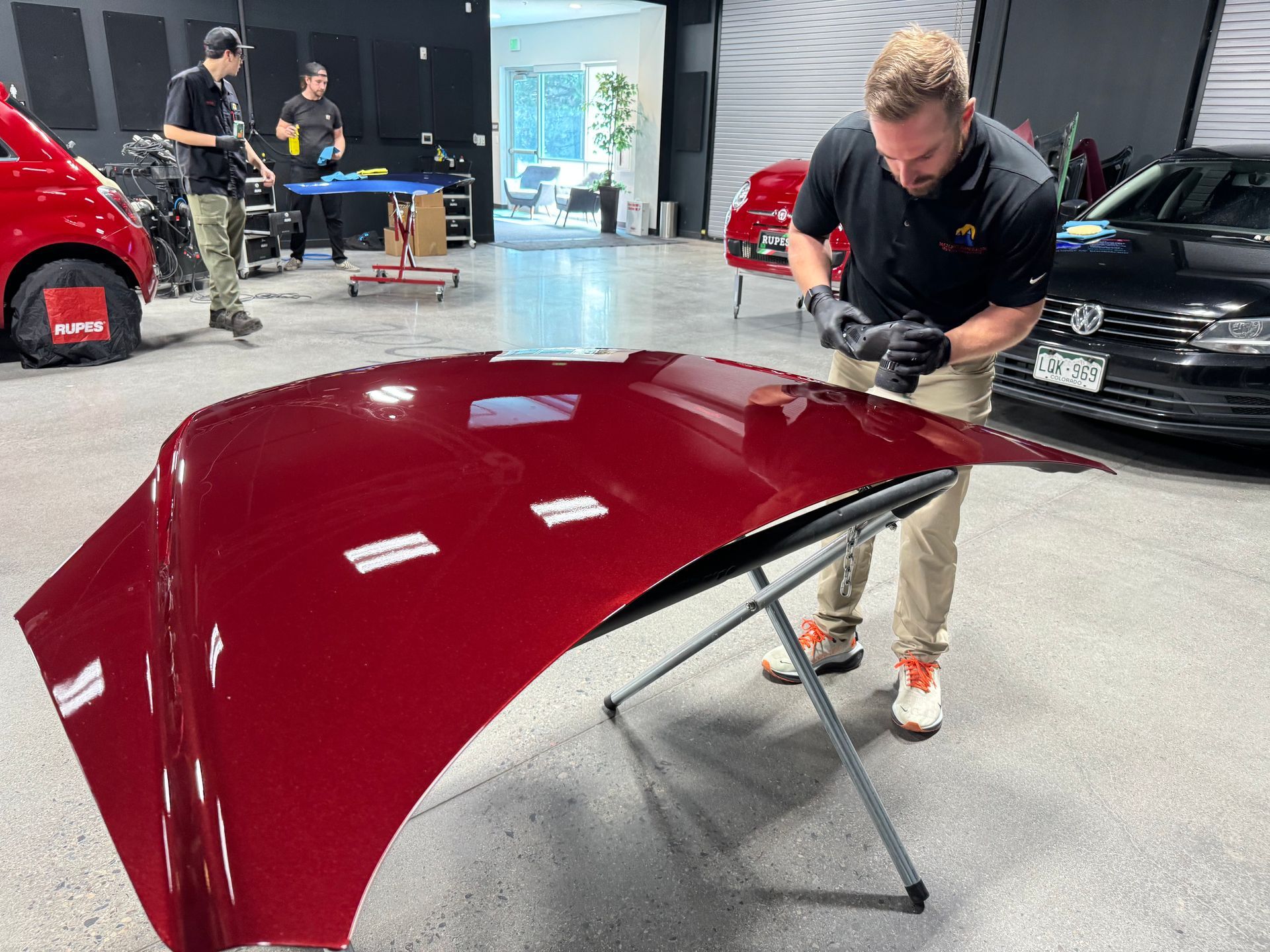A man is working on a red car hood in a garage.