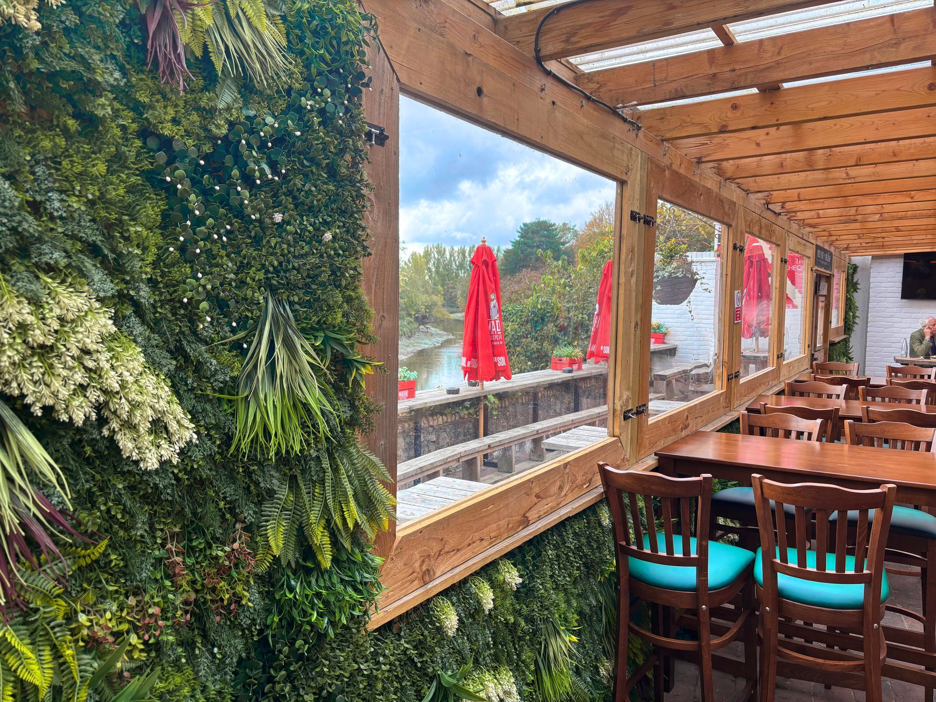 Outdoor dining area with lush greenery, gray and white seating, and glass walls.
