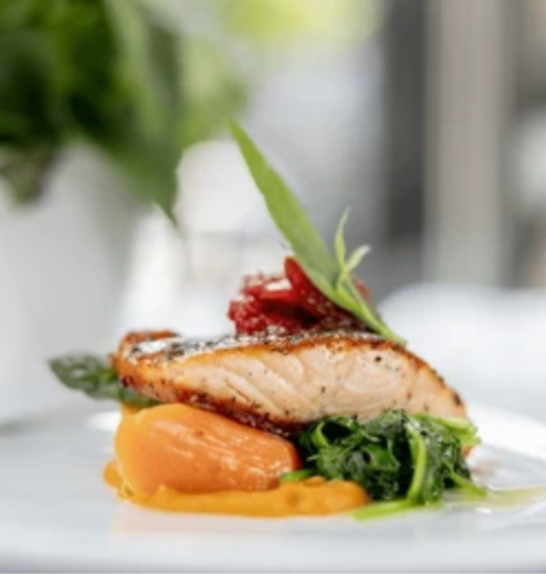 Pan-seared salmon over a bed of puréed sweet potato, spinach, and asparagus, garnished with sundried tomatoes and a leaf.