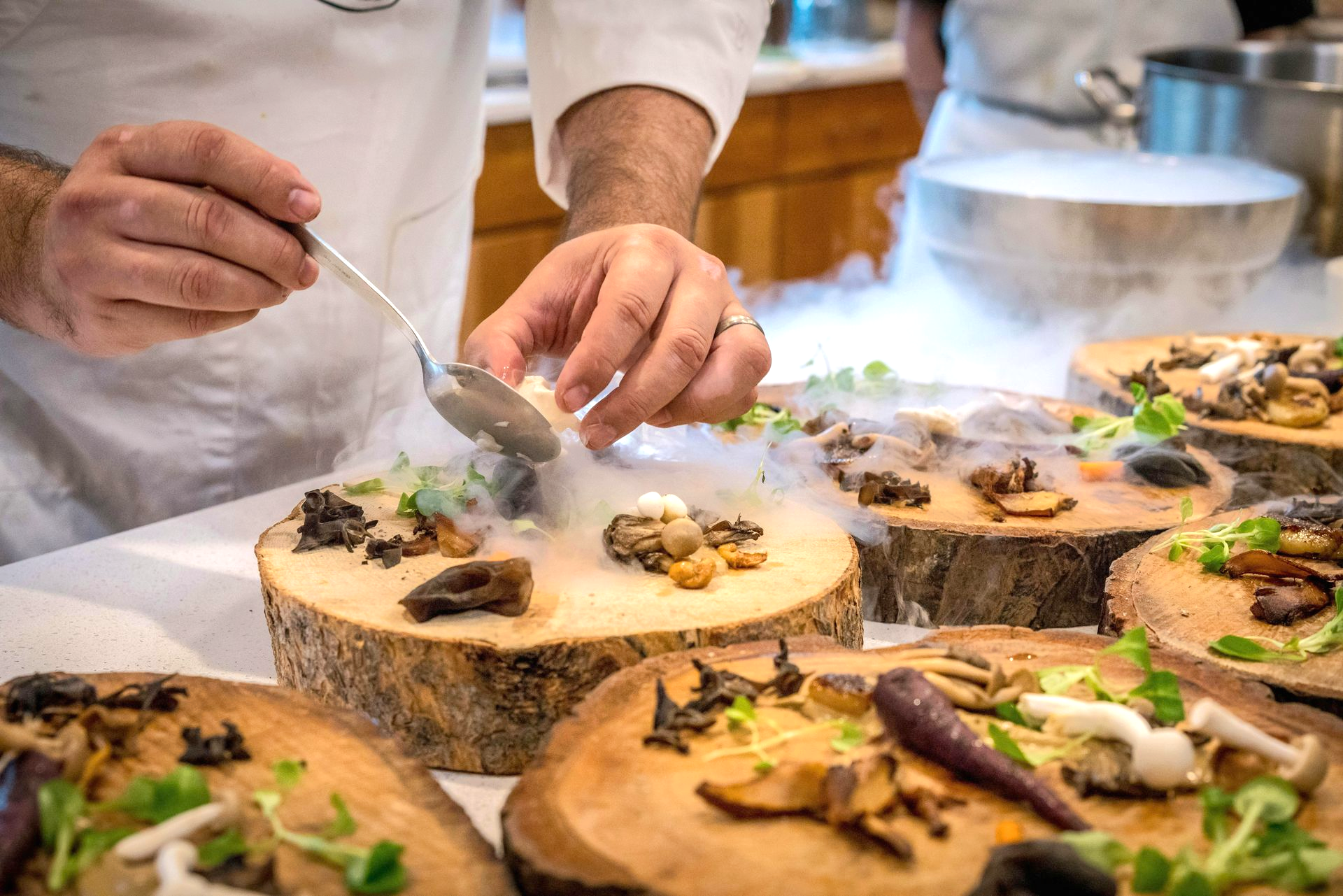 Chef plating mushroom appetizers with dry ice on wooden platters.