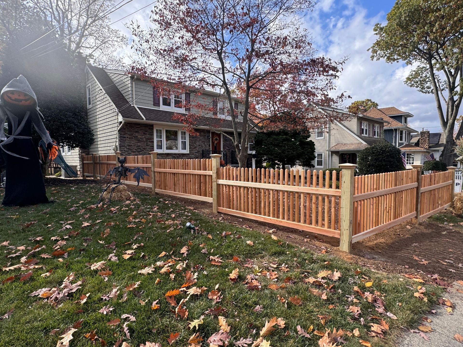 A wooden fence surrounds a lush green lawn in front of a house.