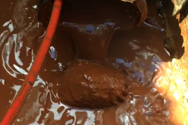 Liquide épais et brun se déversant d'en haut sur une masse plus grande du même liquide.