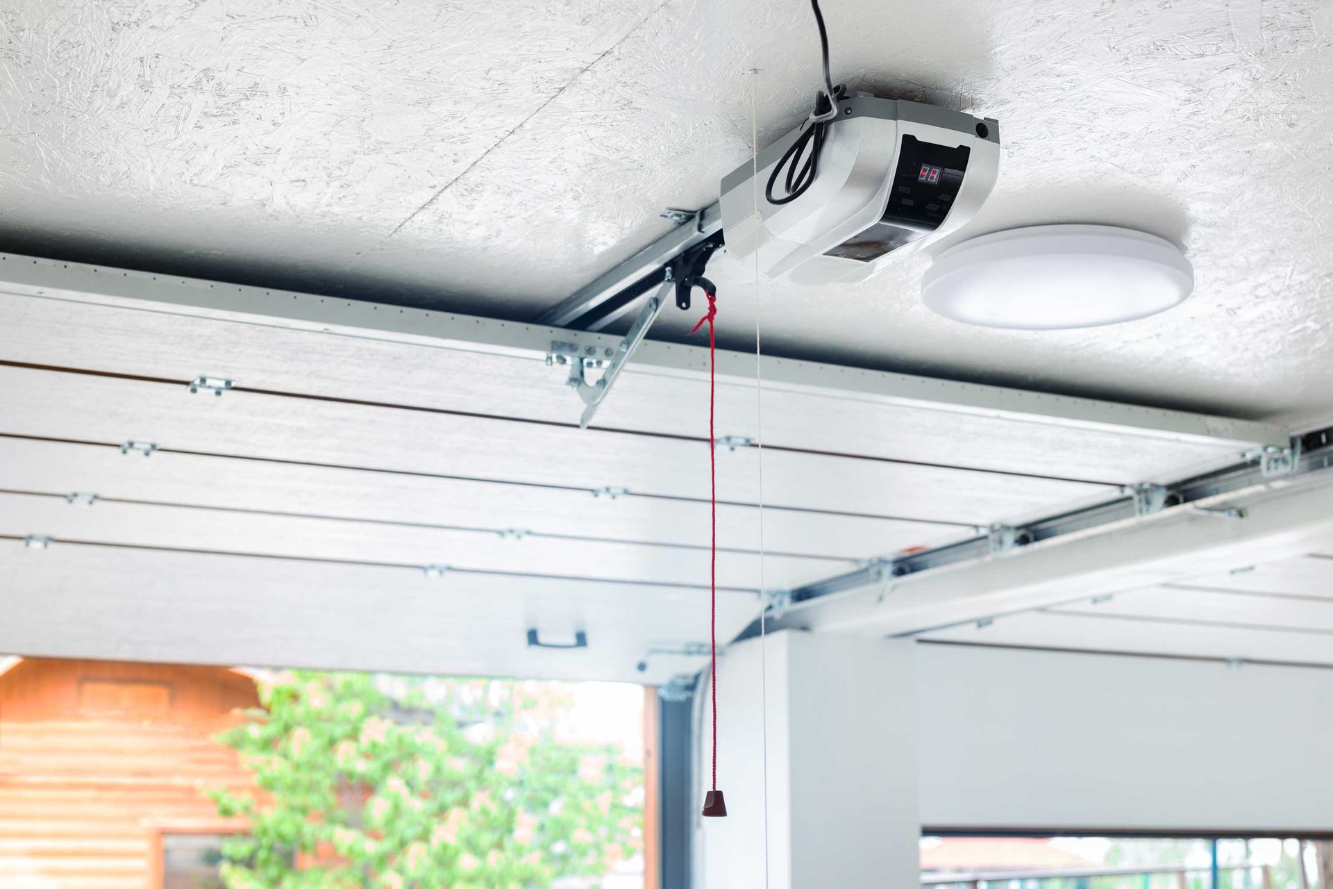 Automatic garage door opener mounted on ceiling with metal rails and pull cord.