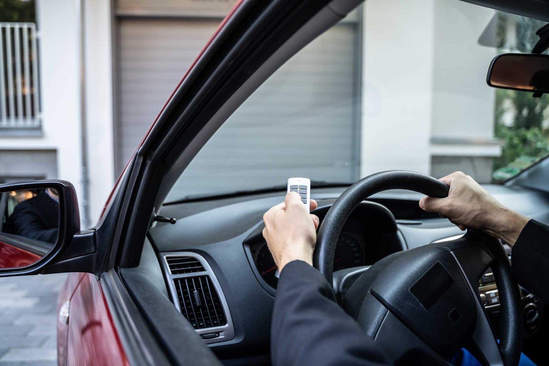 Driver using a remote control inside a car near a garage entrance.