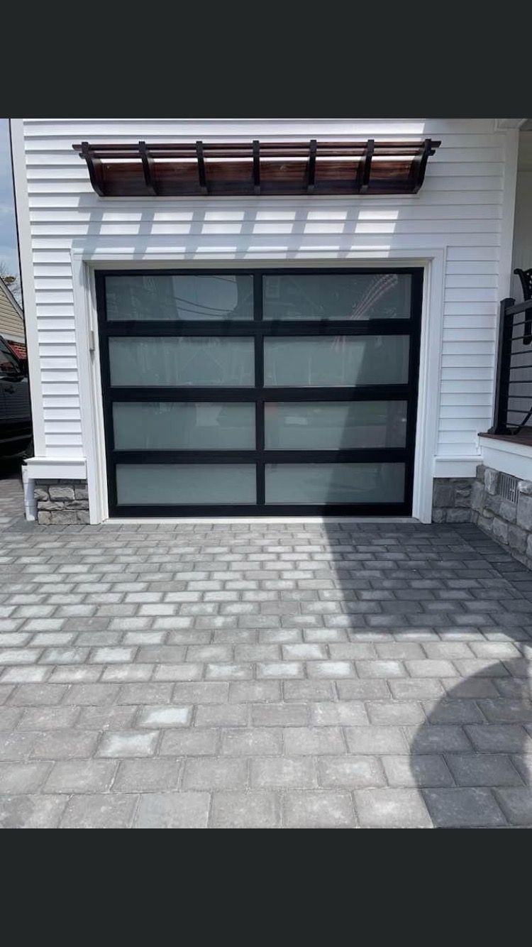 A white house with a black garage door and a brick driveway.