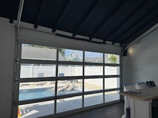 A clear glass garage door opens to a pool area.