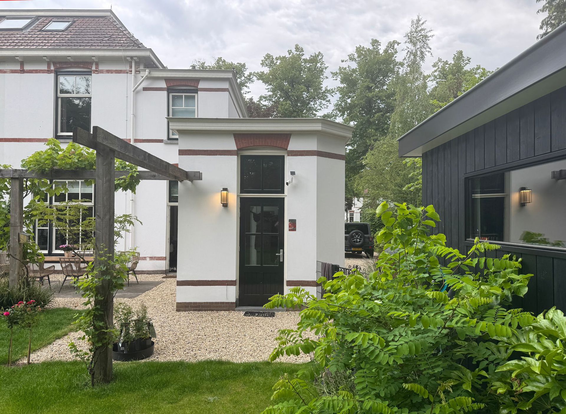 A white house with a black door and a black side building, with a garden in front.