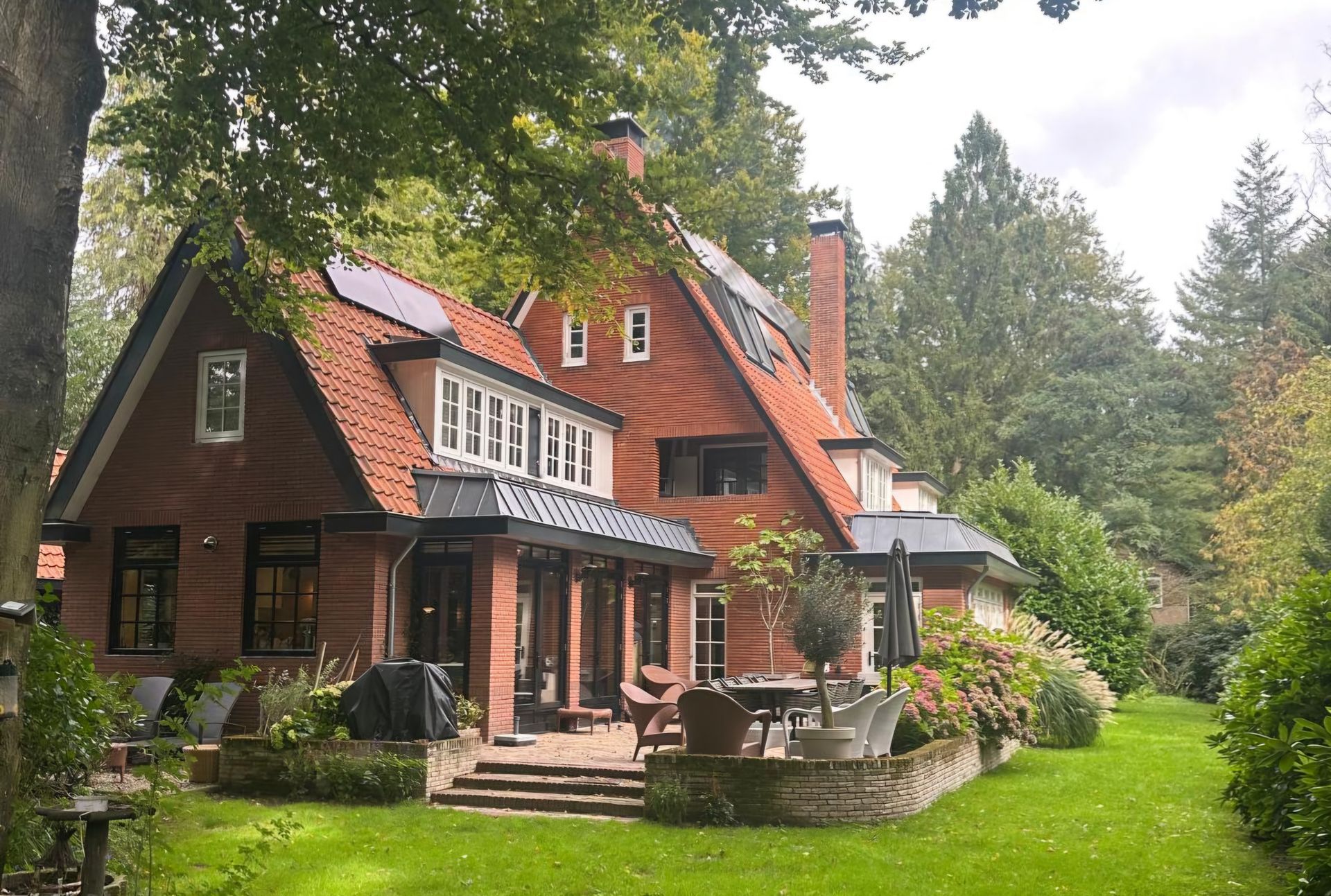 Red brick house with a tiled roof, set in a lush, green garden. Solar panels on roof.