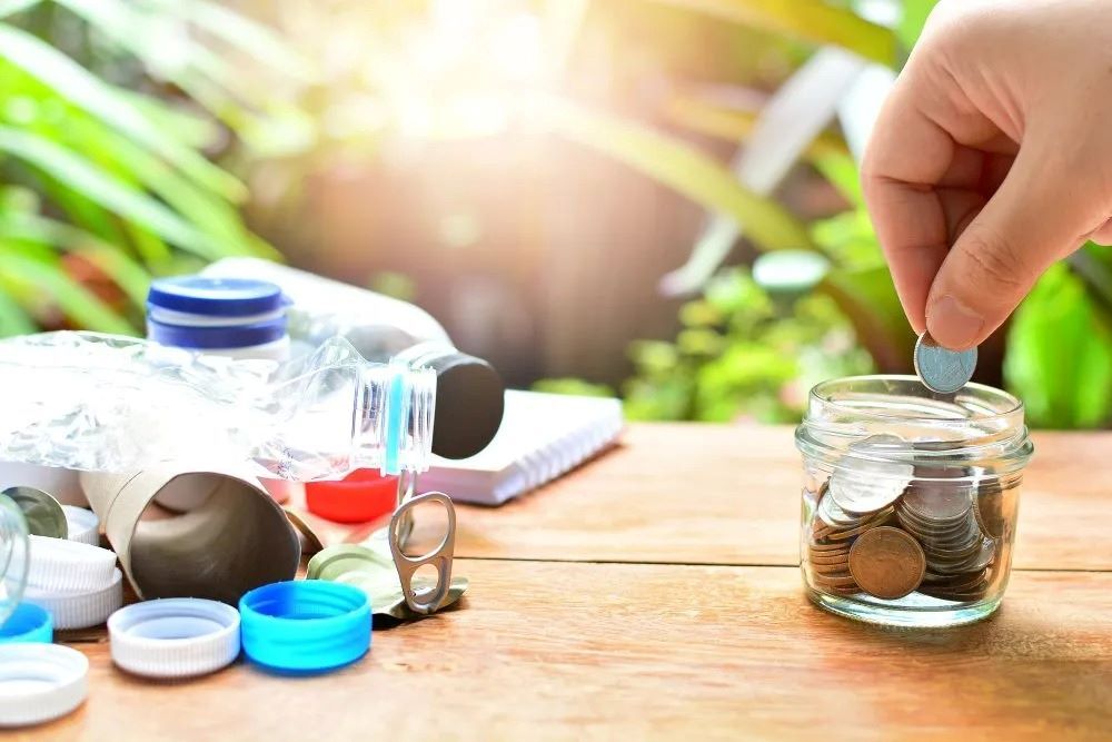 A Person is Putting Coins Into a Jar on a Wooden Table — The Territory Can Man In Winnelie, NT