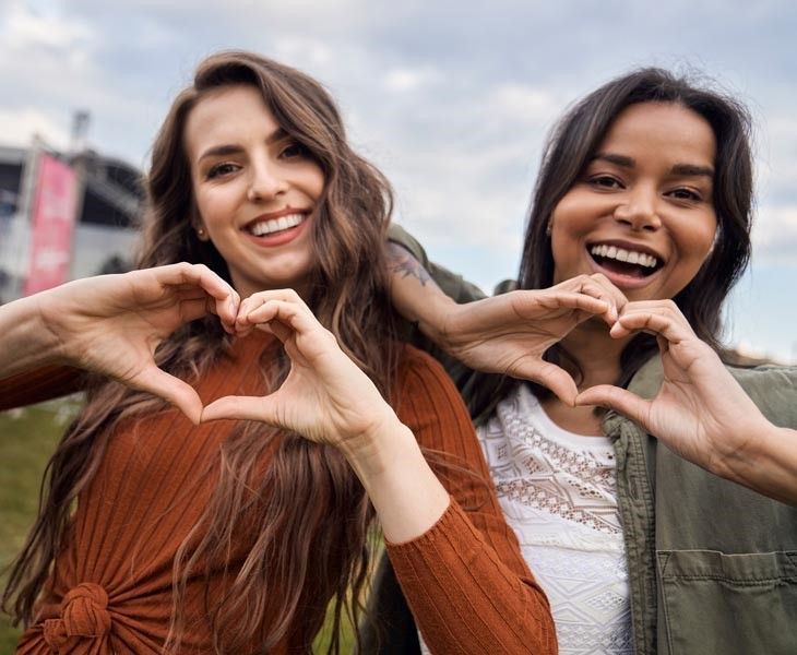 Two women of different cultures making a heart symbol with their hands in celebration of International Women's Day.
