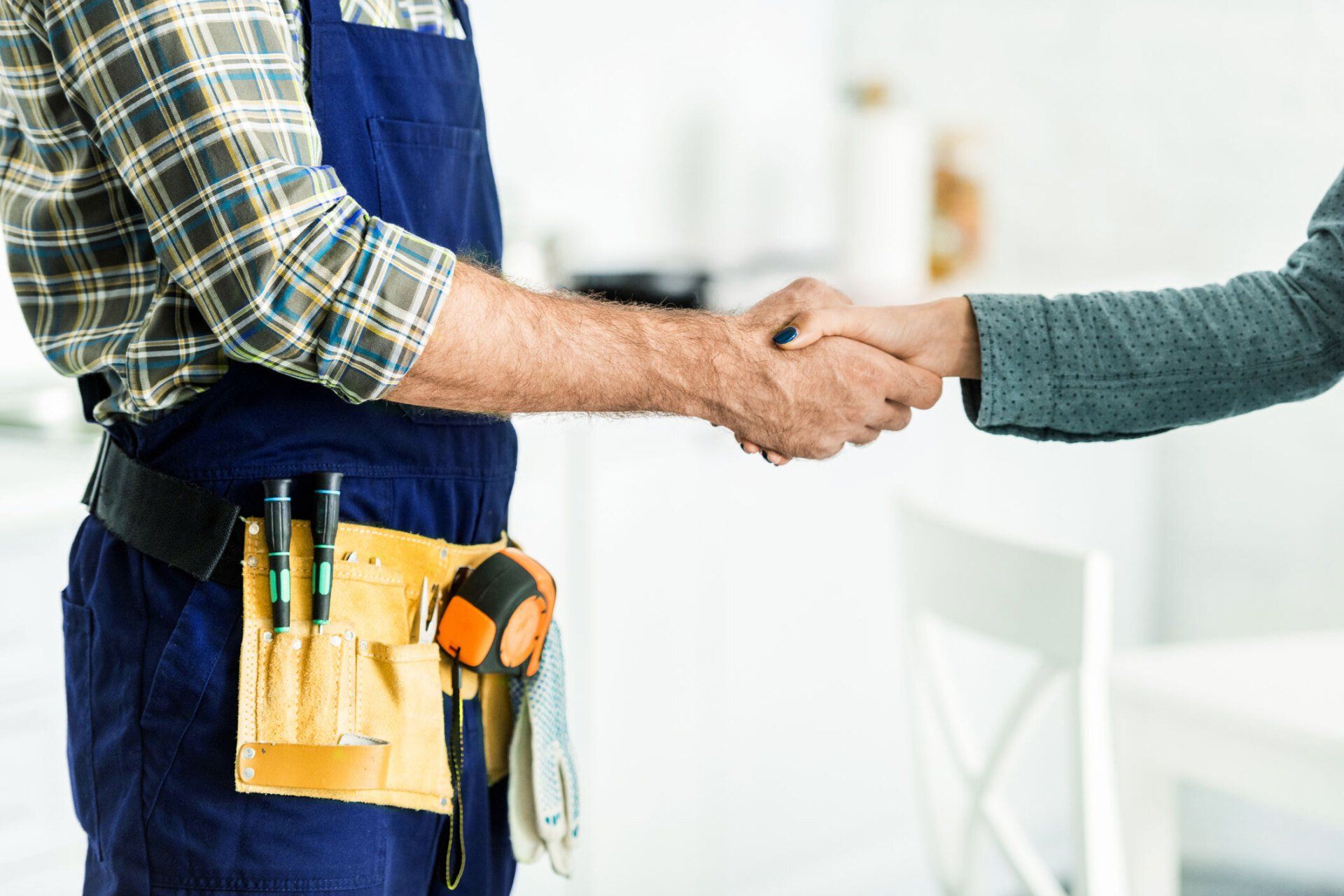 Handshake between repairman in overalls and a person, indoors.