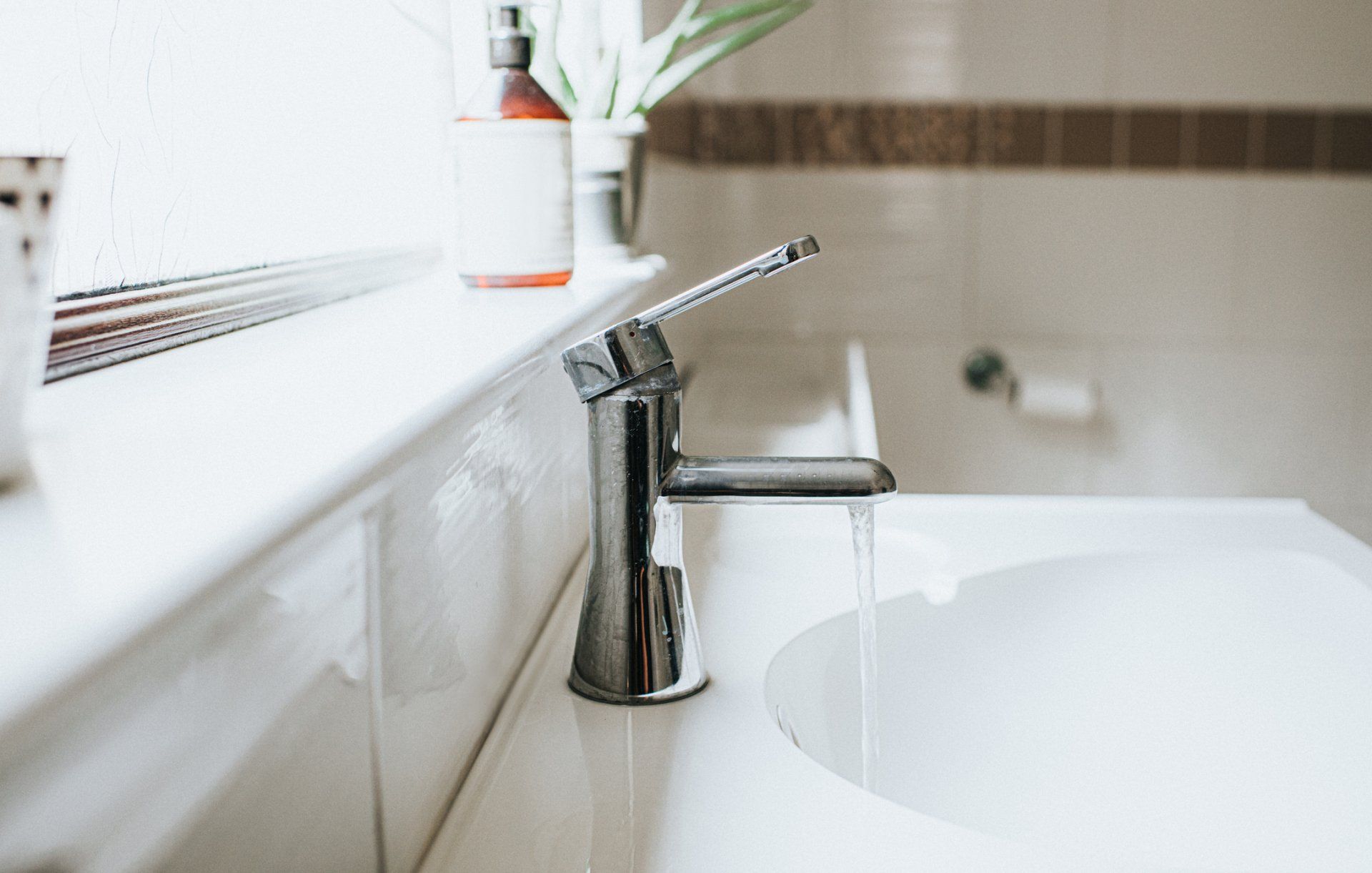 Chrome faucet over a white sink, with water running. A window is behind the sink.