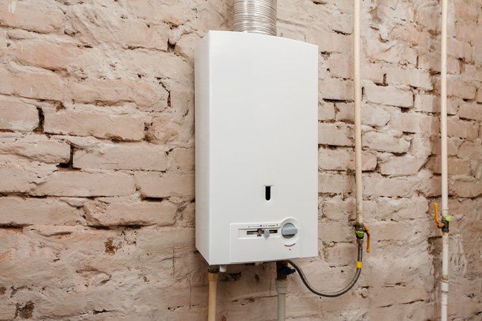 White water heater on a brick wall, with pipes and a vent.