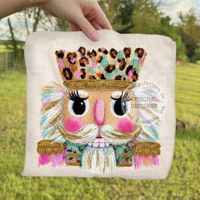 A person holding a tan tote bag embroidered with a colorful, whimsical nutcracker design.