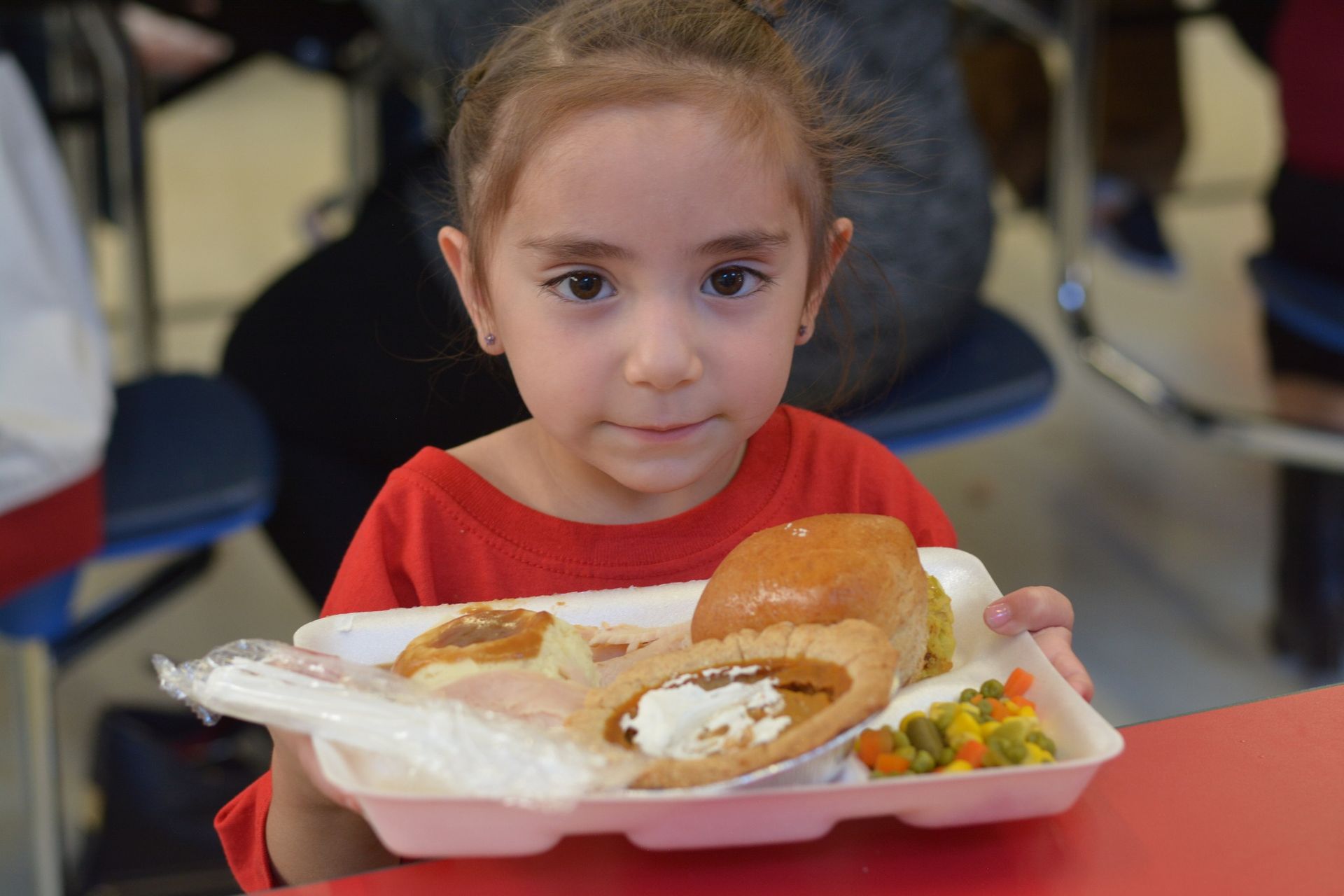 Child holds styrofoam tray with Turkey, mashed potatoes, pumpkin pie, bread and vegetables.