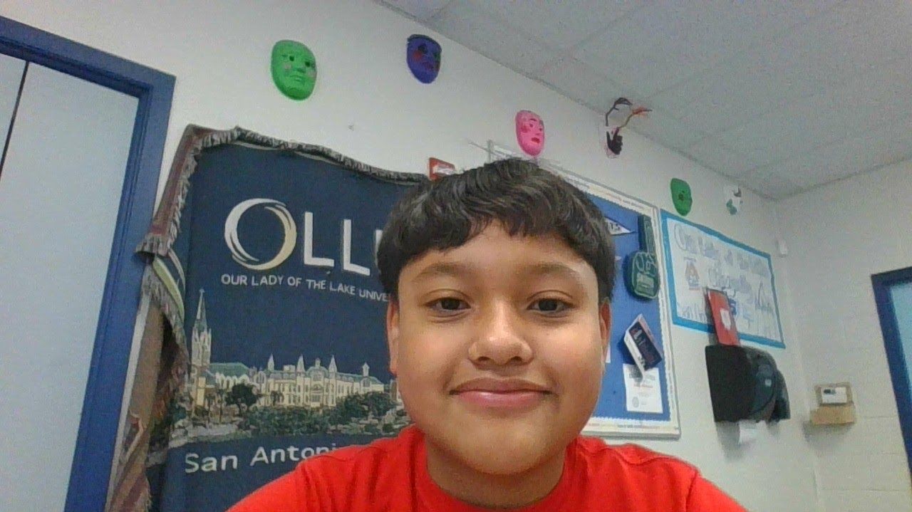 A young boy in a red shirt is smiling in front of a wall with balloons and a banner that says oll