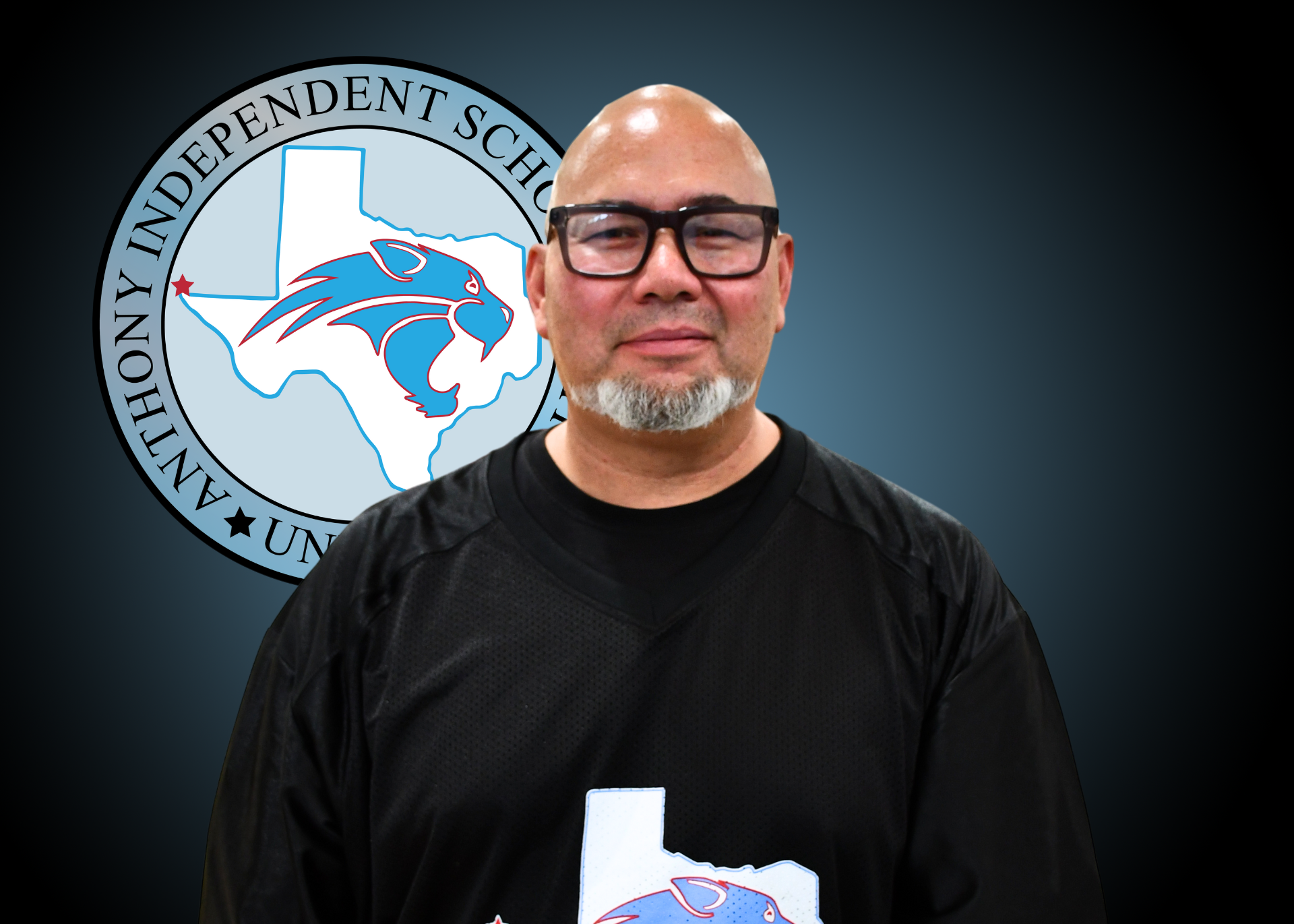 Man wearing black shirt stands in front of Anthony Independent School District logo
