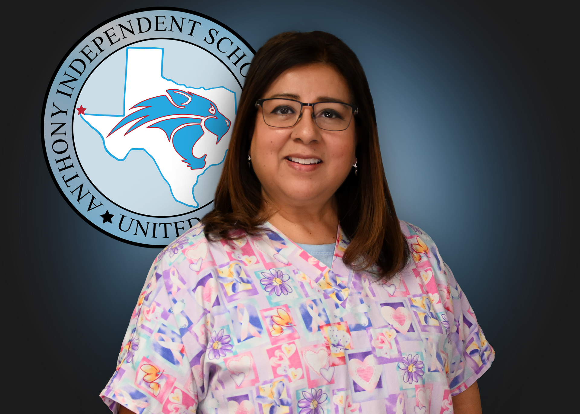 Woman wearing glasses and scrubs stands in front of Anthony ISD logo.