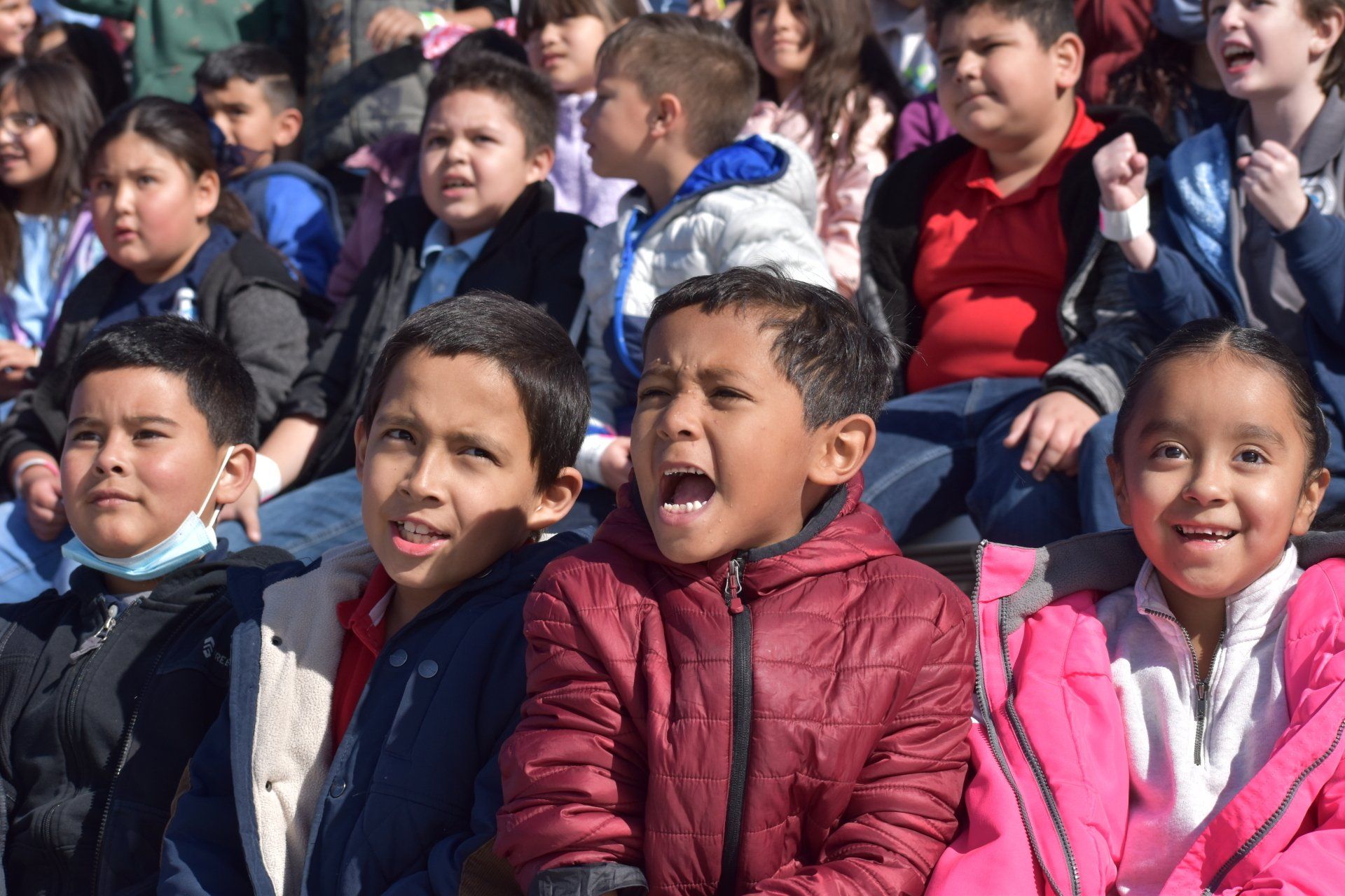 A group of children are sitting in a stadium with their mouths open.