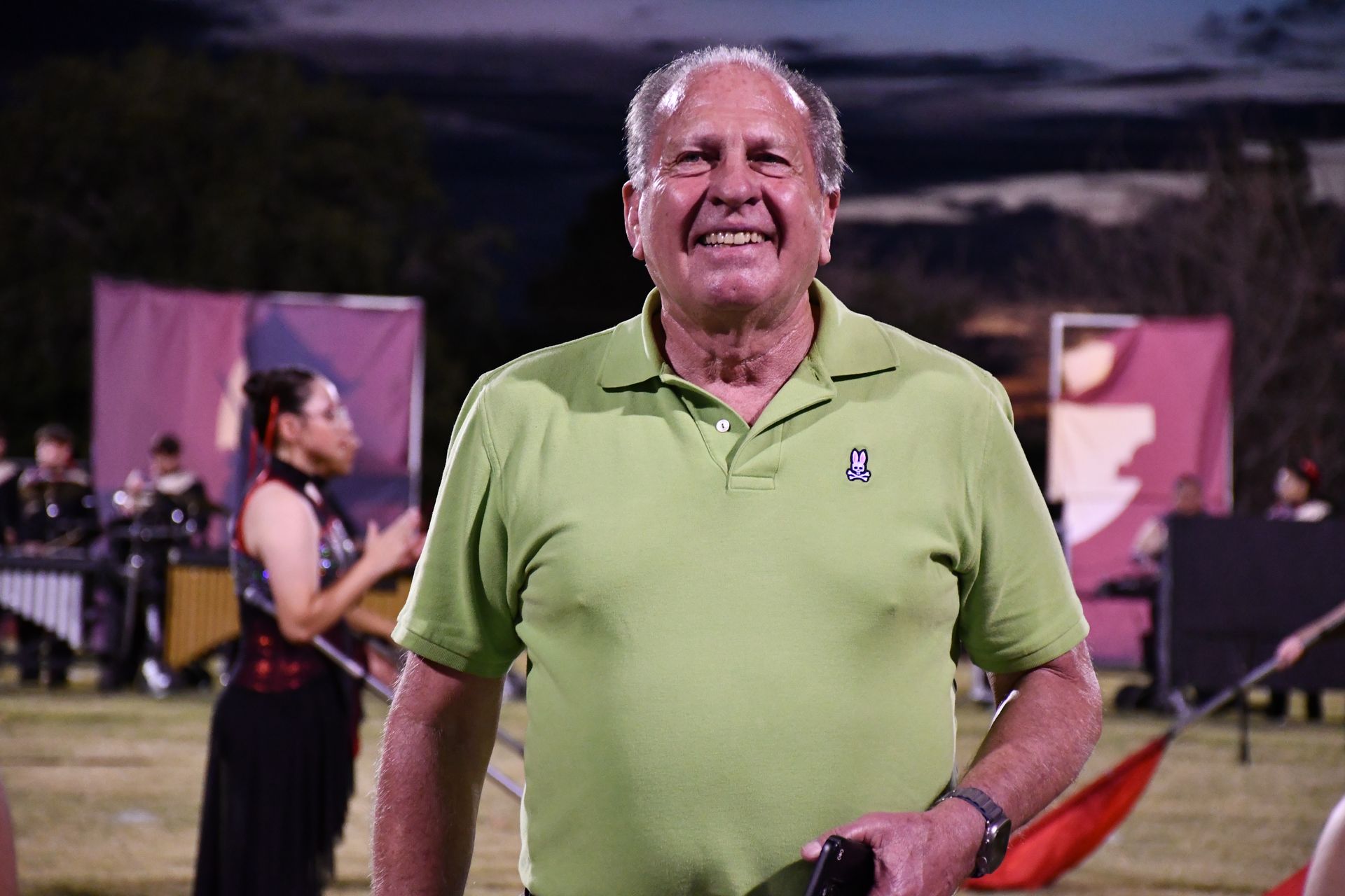 Man wearing gren shirt smiles on football field during halftime show.