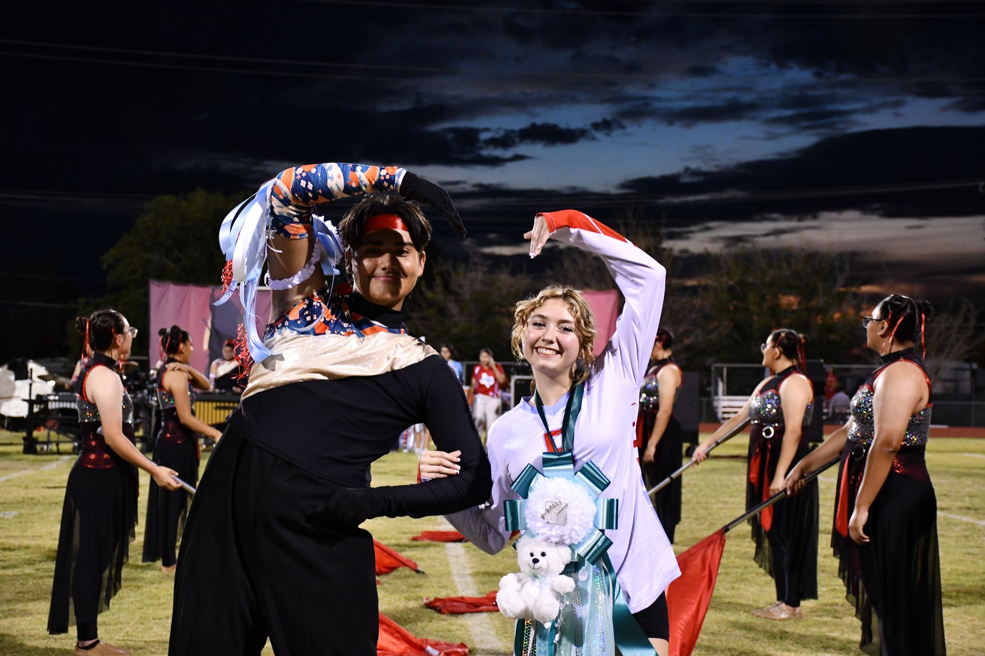 Two students use their arms to create the shape of a heart on the homecoming halftime football field 