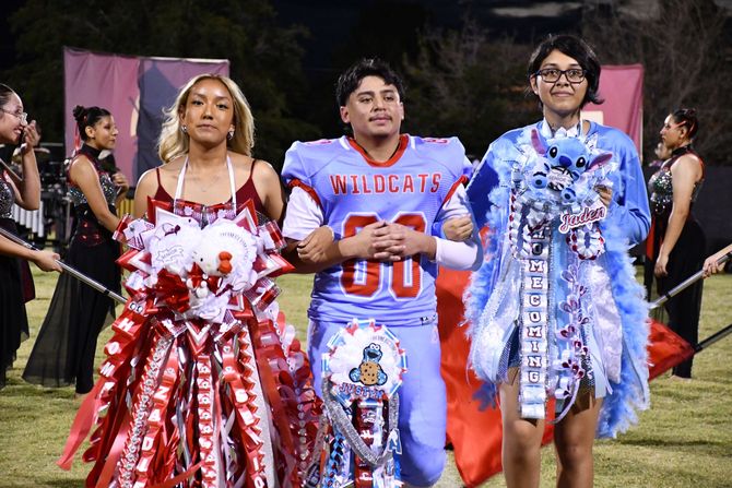 Three students walk down the football field during the homecoming halftime show.