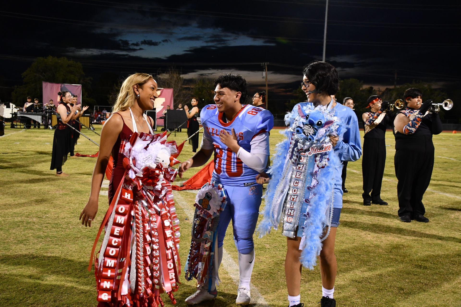 Students smiling on the football field wearing homecoming mums. The three of them were nominated for Homecoming Queen and King