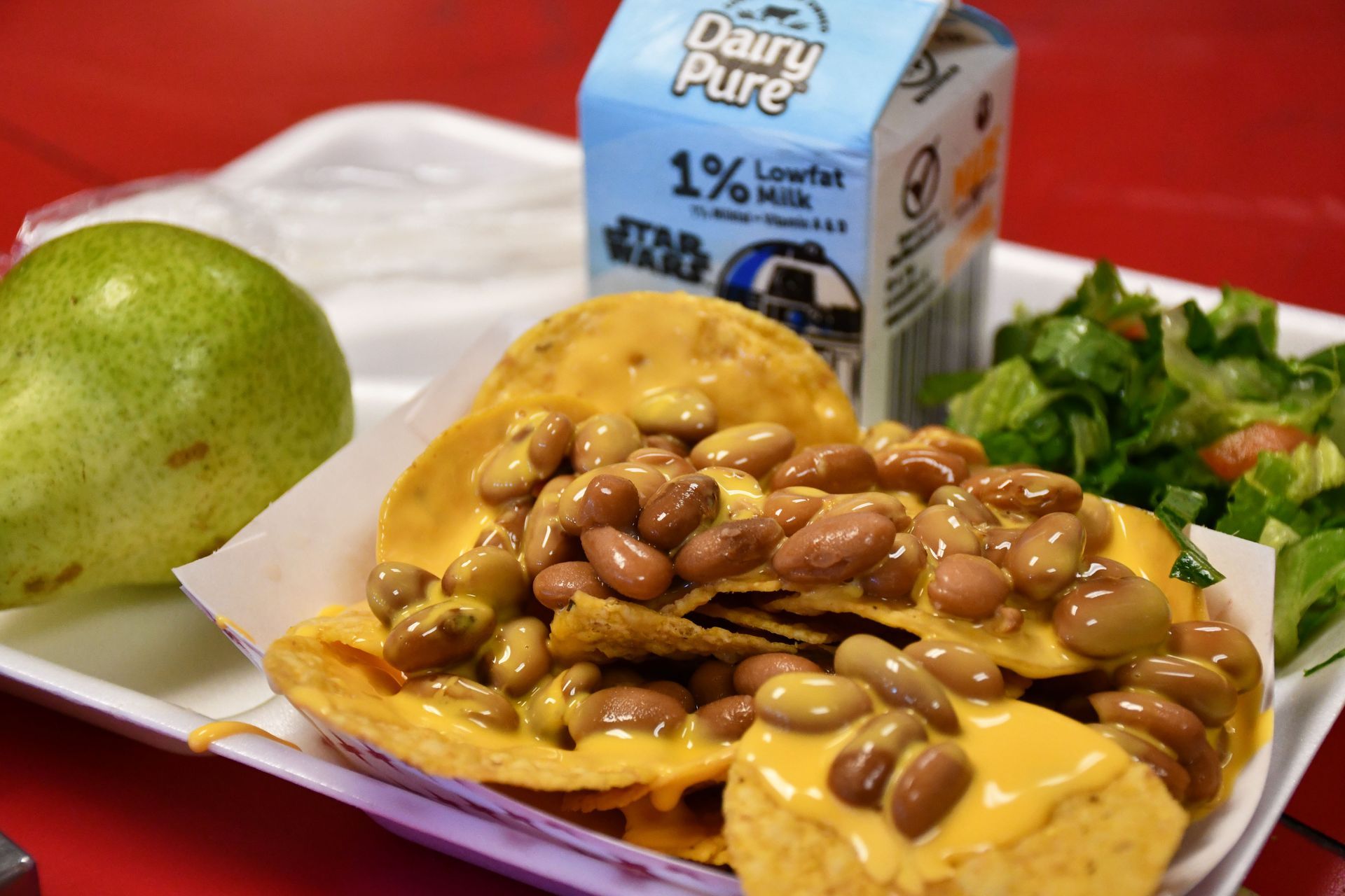 Nachos drenched in cheese and beans with a pear, milk and side salad.