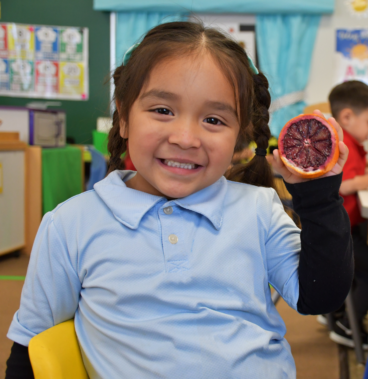 Child smiling at camera holding up a fruit