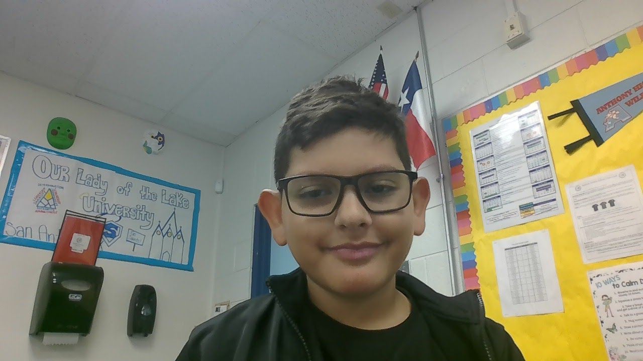 A young boy wearing glasses is standing in front of a bulletin board.