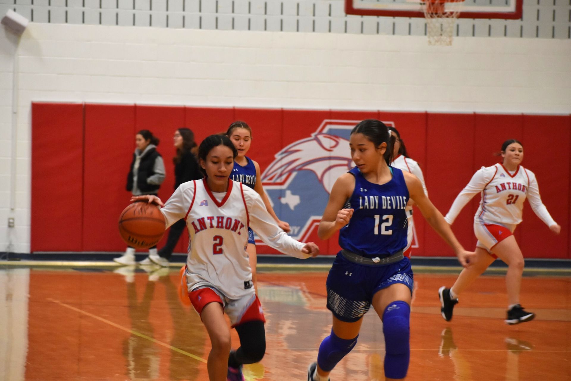 Anthony female basketball player dribbles the ball while her opponent runs next to her.
