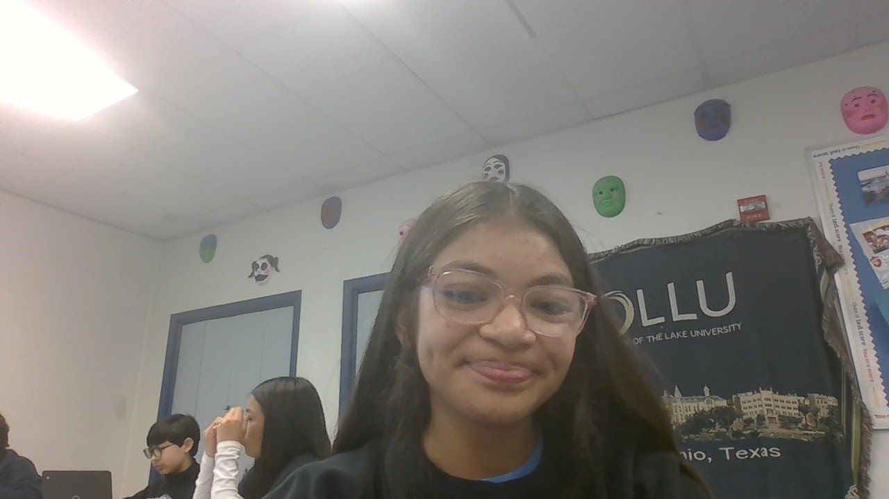 A girl wearing glasses is smiling in a classroom.