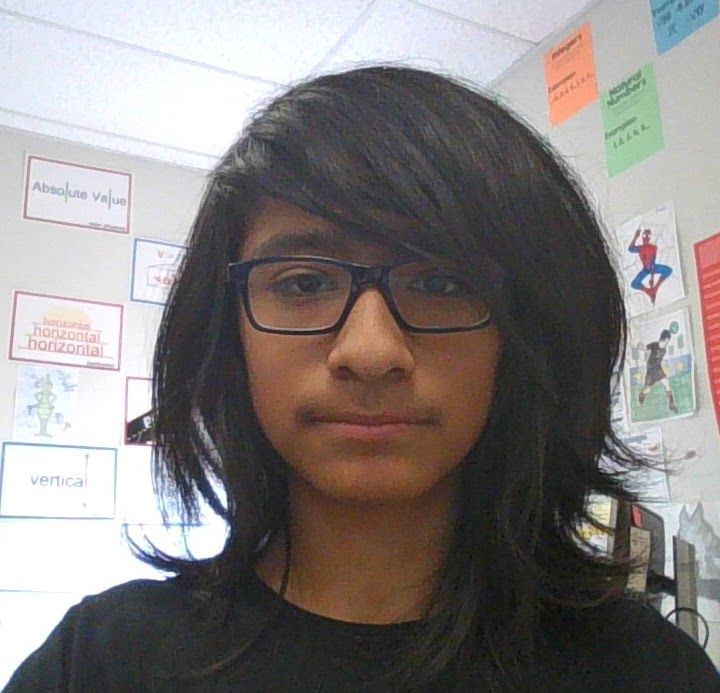 A young man wearing glasses stands in front of a wall with sticky notes on it