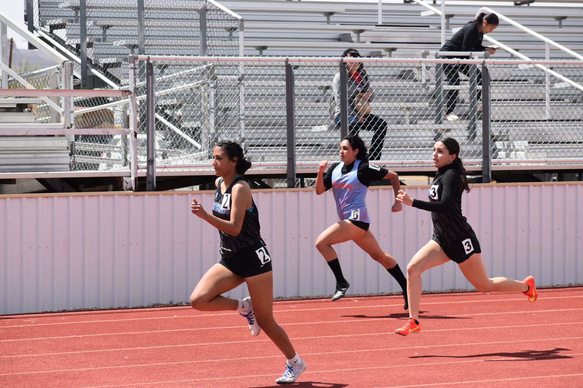 Three student athletes sprint on a track. The Anthony ISD student is in between the other two students.