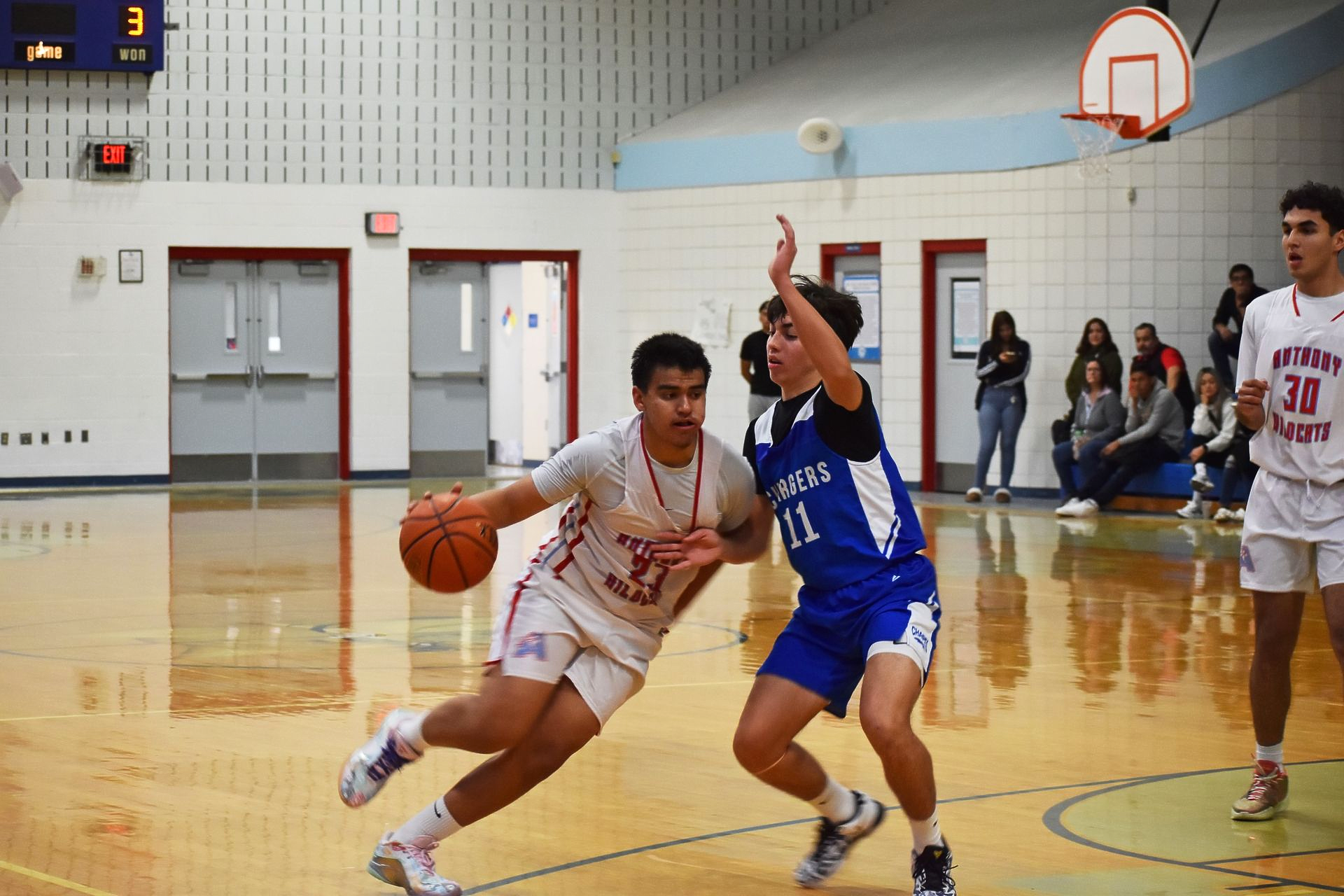 Anthony baskeball player dribbles the ball with his right hand while he blocks the opposing team with his left hand.