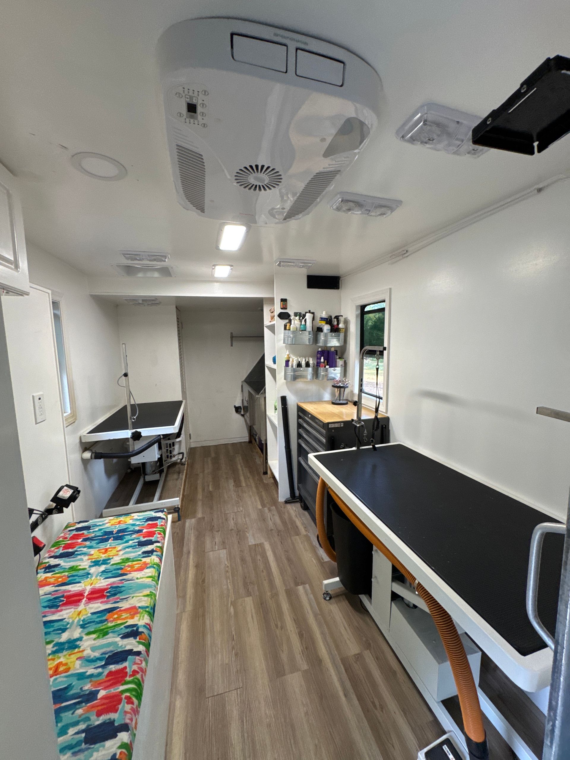 Inside of a mobile pet grooming trailer with grooming tables, bathtub, and storage.