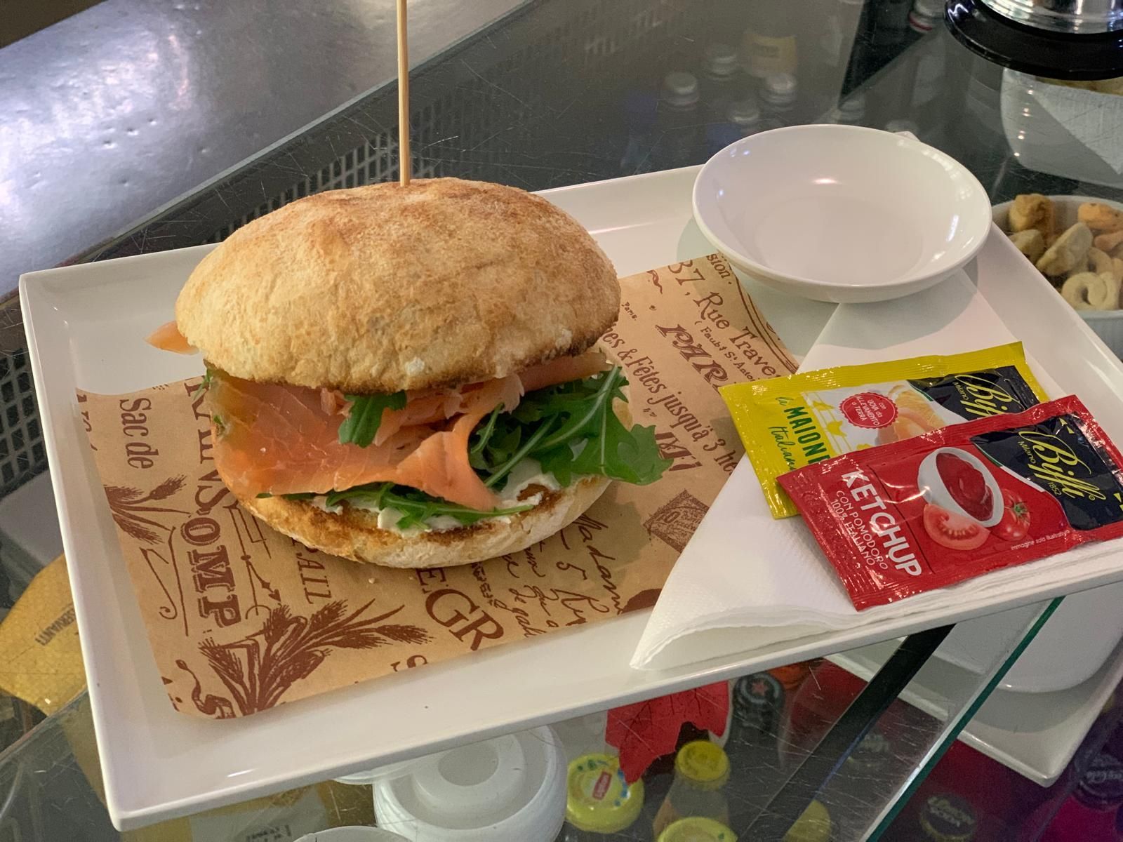 Un panino è seduto su un piatto bianco accanto a una ciotola di ketchup.