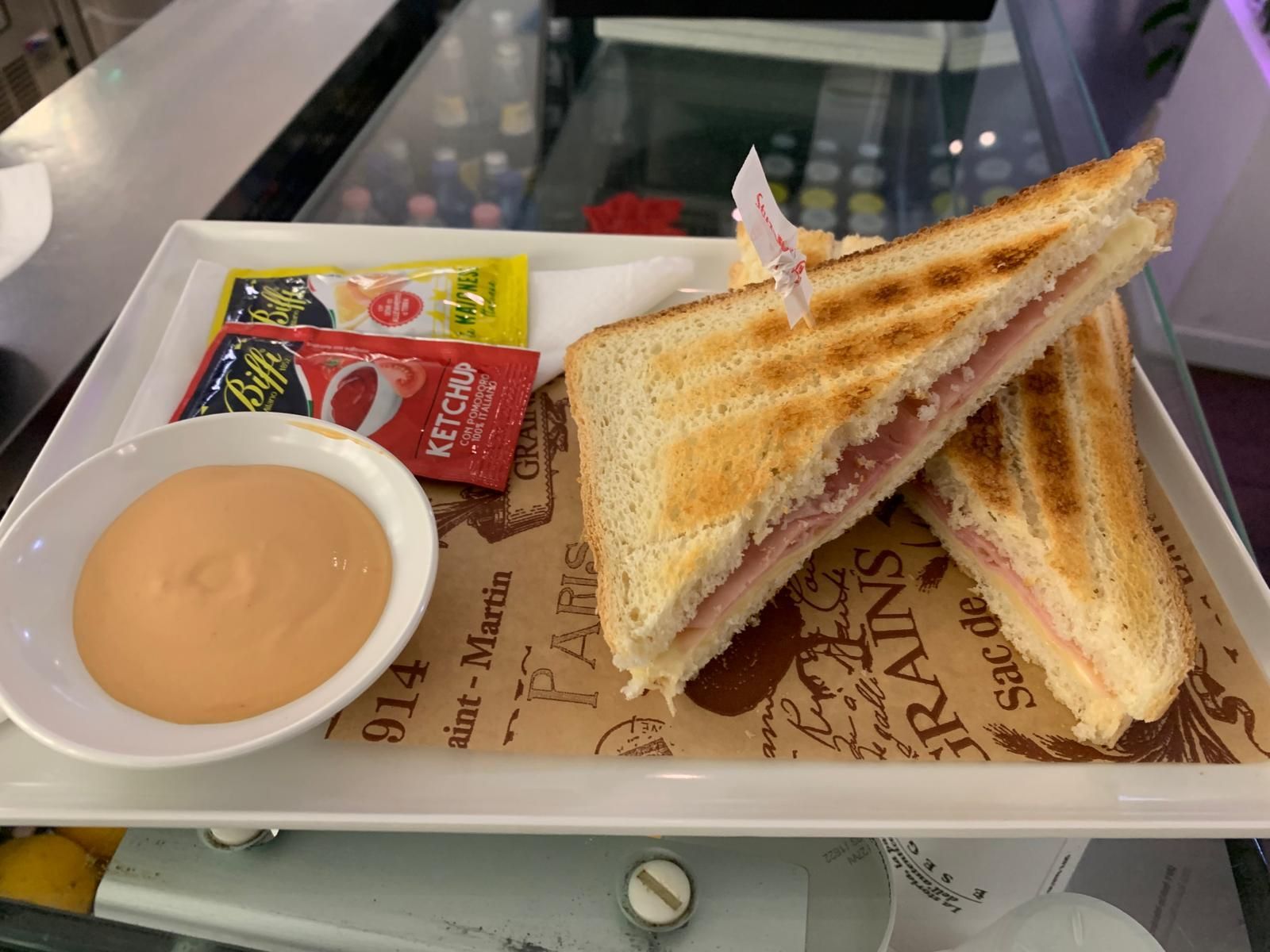 C'è un panino su un piatto con ketchup e salsa.