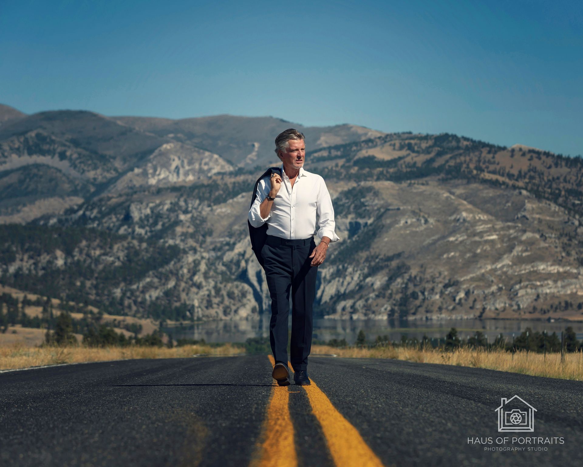 Man standing on a road with yellow lines, holding a bottle, with mountains in the background.