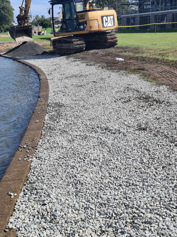 Excavator Moving Rocks Beside Water — Projects in Coopernook, NSW