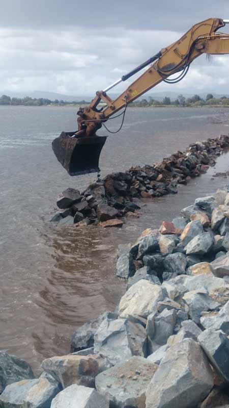 Excavator Carrying Creating Rock Barrier In Water — Projects in Coopernook, NSW