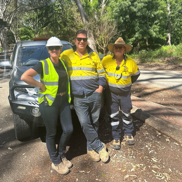 Three construction workers are posing for a picture in front of a truck.