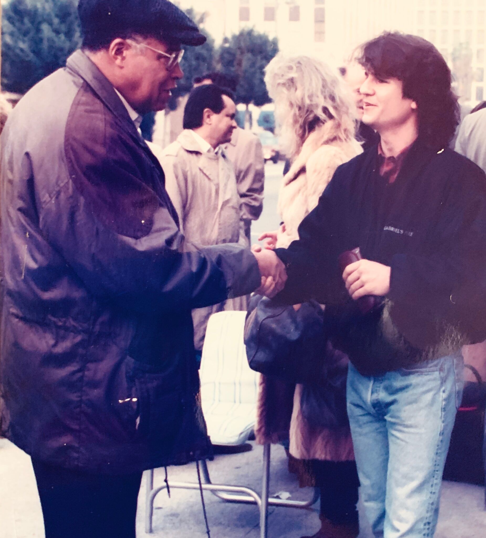 A man in a purple jacket shakes hands with another man