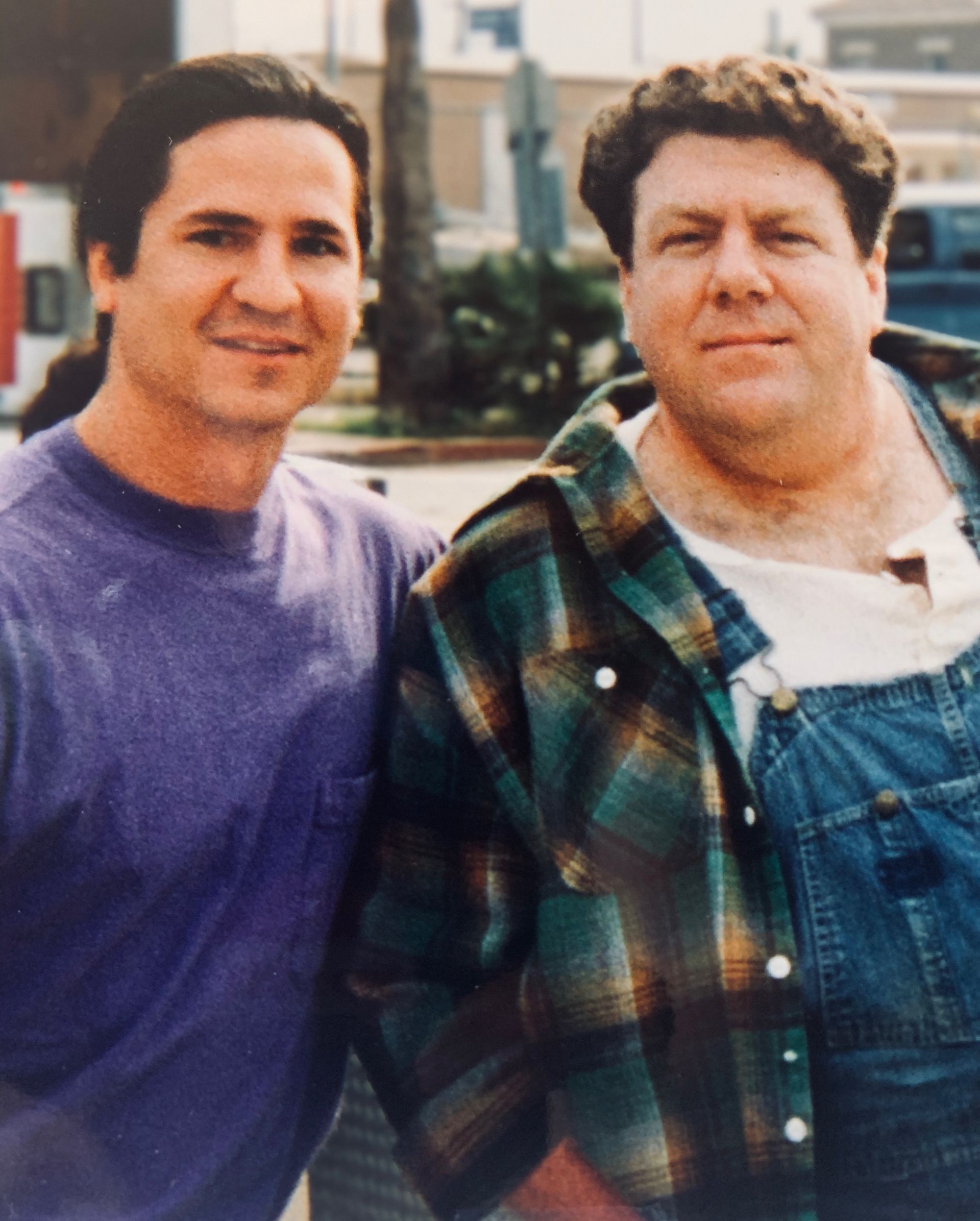 Two men are posing for a picture and one is wearing overalls