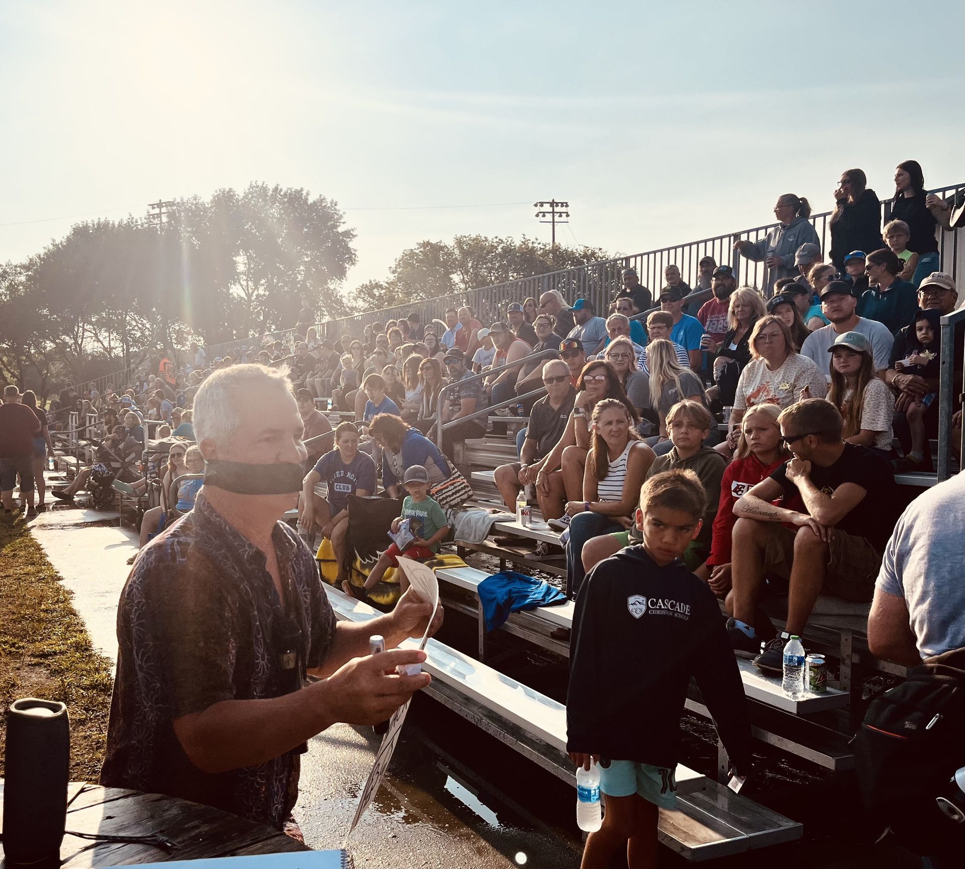 A man is standing in front of a crowd of people sitting on bleachers.