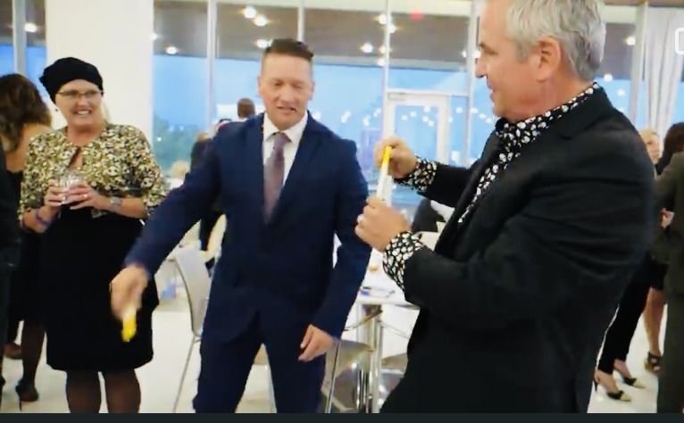 A man in a suit and tie is holding a yellow object in front of a group of people.