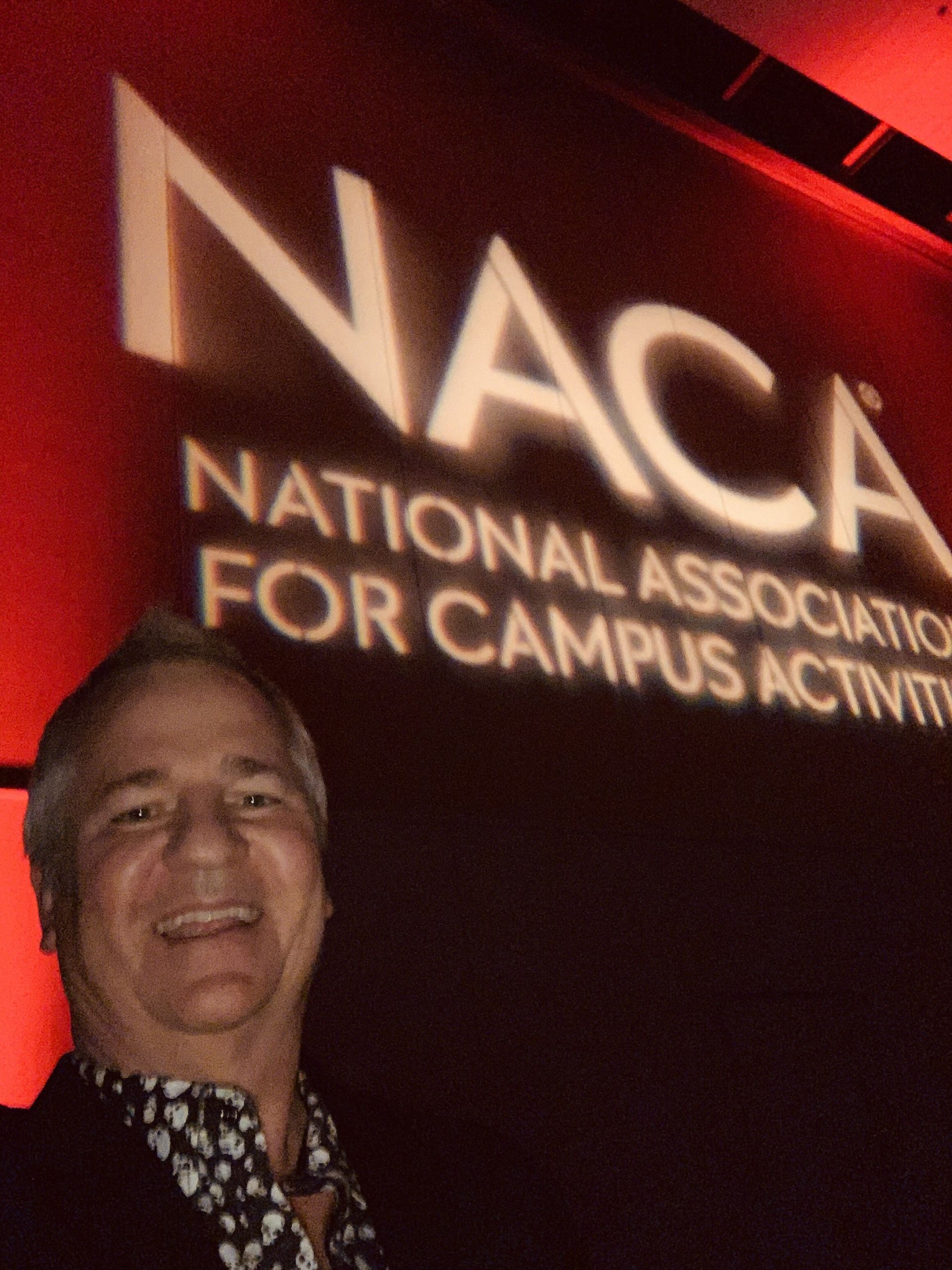 A man stands in front of a national association for campus activities sign