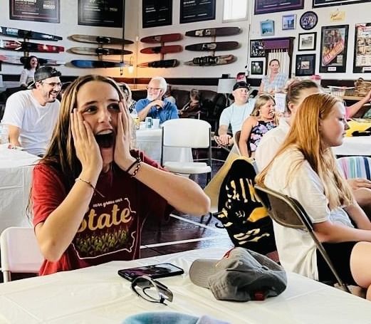 A woman wearing a state shirt is sitting at a table with other people