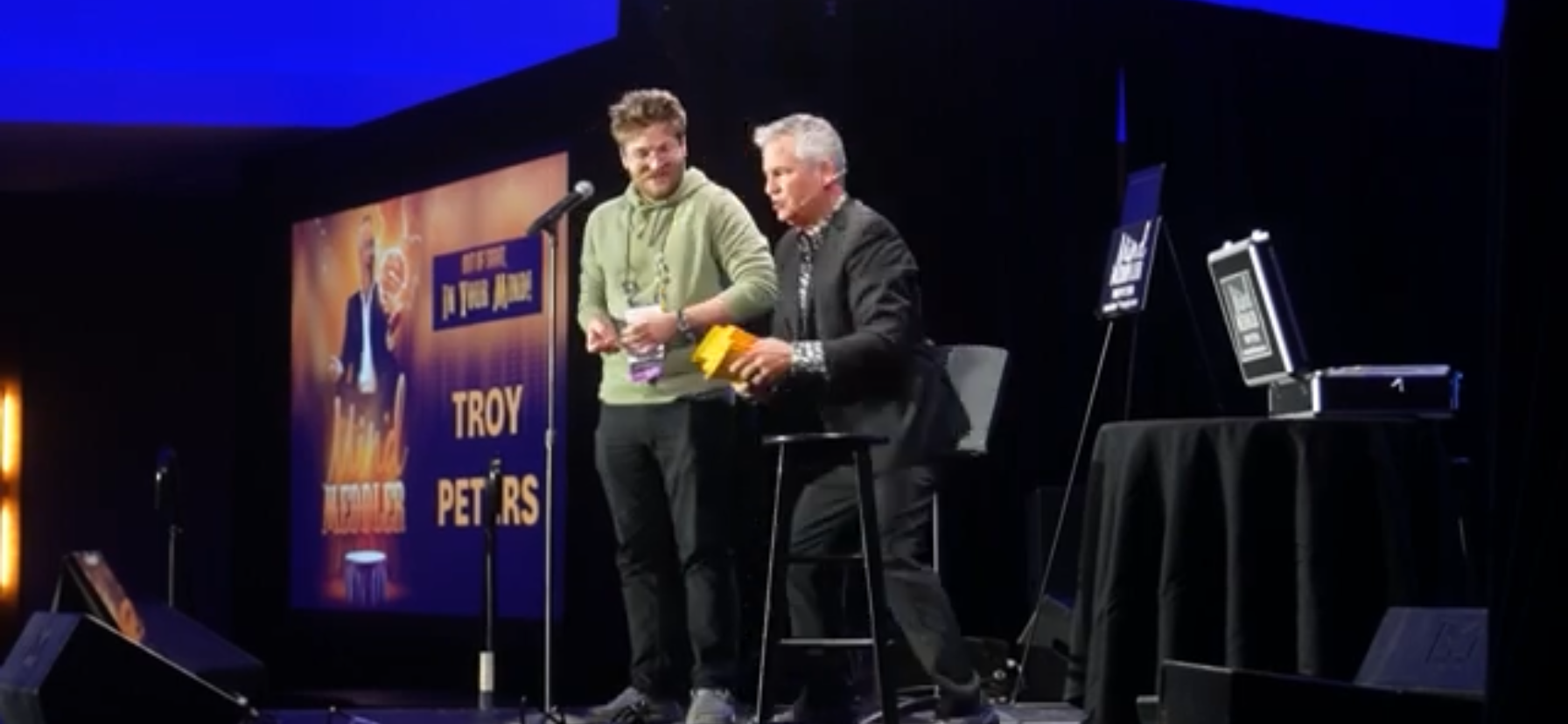 Two men are standing on a stage talking into microphones.